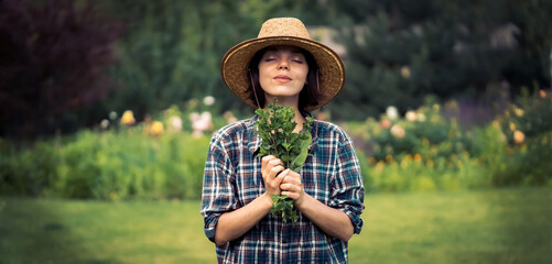 A young girl gardener in a straw hat holds a bouquet of harvested fresh mint.