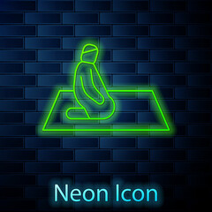 Glowing neon line Muslim man prays on the carpet icon isolated on brick wall background. Vector