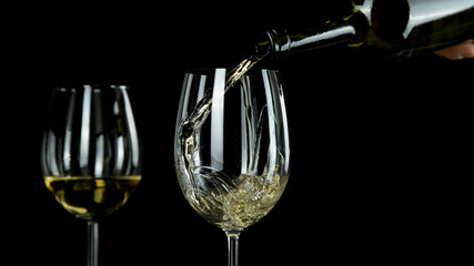 Pouring white wine, black background. Back view.