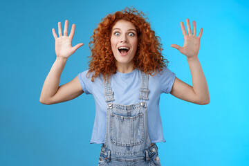 Excited crazy playful funny redhead curly emotive girl yelling carefree raise hands surrender up open mouth fool around smiling broadly stare camera joyful express wild daring emotions - obrazy, fototapety, plakaty