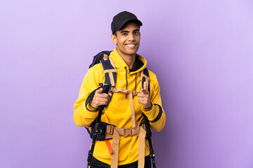 African American man with backpack and trekking poles over isolated background pointing to the front and smiling