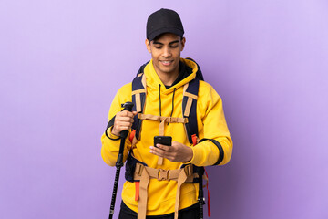 African American man with backpack and trekking poles over isolated background sending a message with the mobile