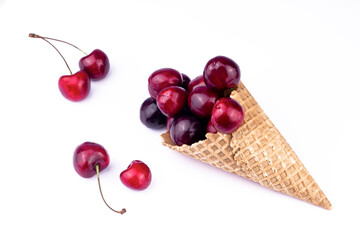 Fresh red cherries in waffle cone. Ice cream cone with ripe sweet cherry on white background with copy space. Summer creative concept flat lay. Top view.
