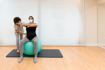 Obraz premium Physiotherapist helping a pregnant woman to exercise sitting on a fitness ball
