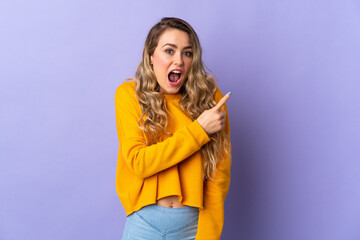 Young Brazilian woman isolated on purple background surprised and pointing side