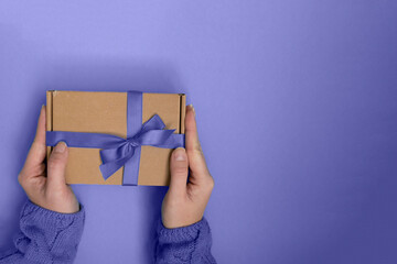 hands holding gift box with purple ribbon bow on purple background. present for Christmas, new year, valentine day