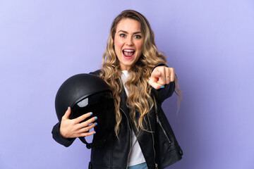 Young Brazilian woman holding a motorcycle helmet isolated on purple background surprised and pointing front