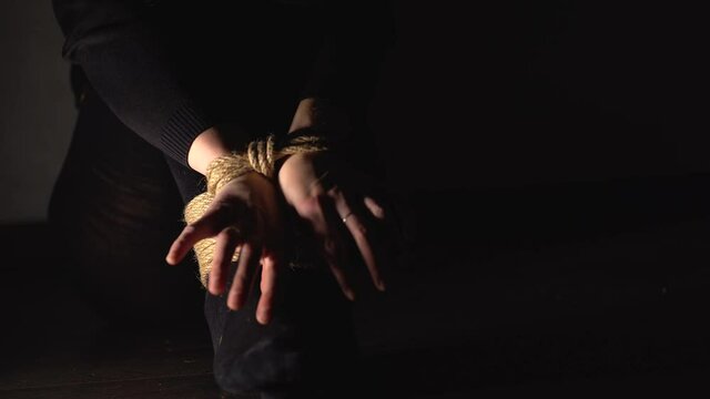 Woman is trying to free her hands and feets from rope. Human Trafficking. Domestic violence