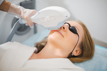 Close up of a young woman face while cosmetologist does the procedure for laser hair removal of unwanted hair of the face and upper lip in a beauty salon