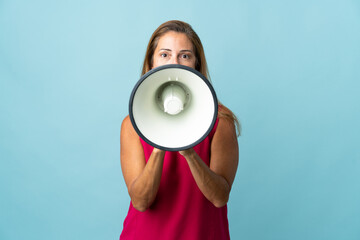 Middle age brazilian woman isolated on blue background shouting through a megaphone