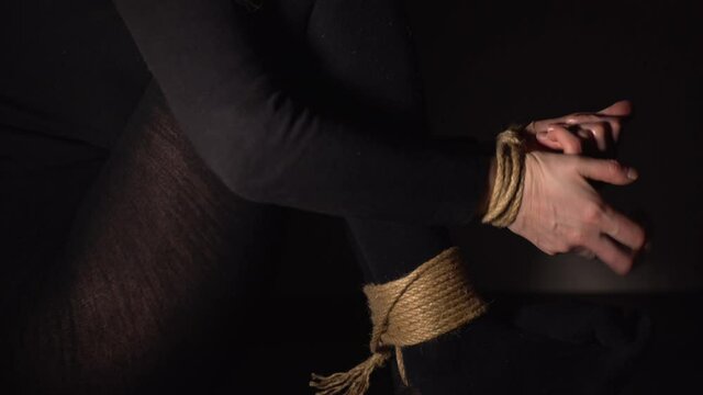 Woman is trying to free her hands and feets from rope. Human Trafficking. Domestic violence