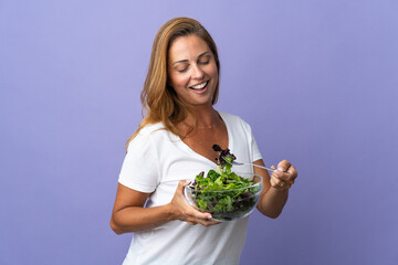 Middle age brazilian woman isolated on purple background holding a bowl of salad with happy expression