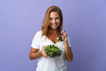 Middle age brazilian woman isolated on purple background holding a bowl of salad with happy expression
