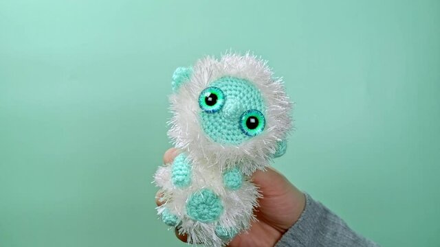 Dancing Yeti Bigfoot In Hands. Handmade Crocheted Soft Toy. Surf Green Background. 4K