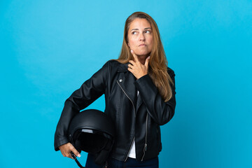 Middle age woman holding a motorcycle helmet isolated on blue background looking up while smiling