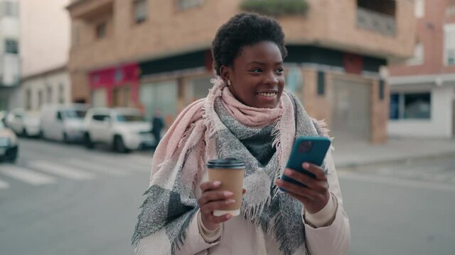 Young african american woman using smartphone and drinking coffee at street