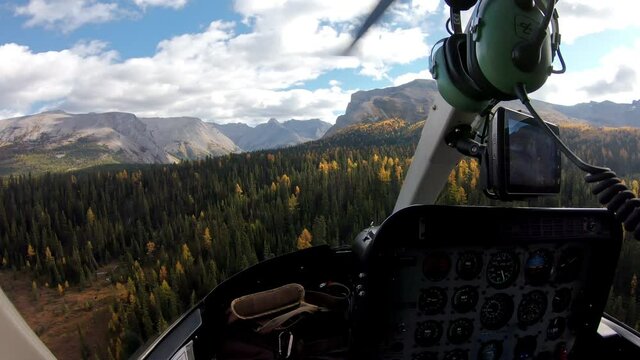 Inside of pilot flying a helicopter on autumn forest in rocky mountains