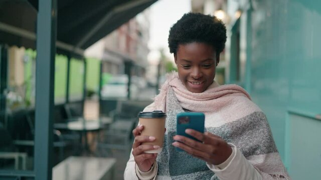 Young african american woman using smartphone and drinking coffee at street