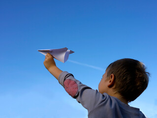 A little boy dreams of flying on an airplane and holds a paper plane in his hands and looks at the...