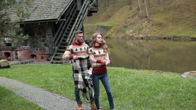 Caring boyfriend brings checkered plaid to his girlfriend. Young couple hugging near the river in the countryside. Beautiful couple in the autumn village.