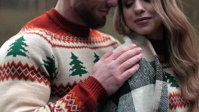 Happy couple wearing identical sweaters enjoying their date. Man caressing his girlfriend covered with plaid. Dating couple at the nature backdrop.