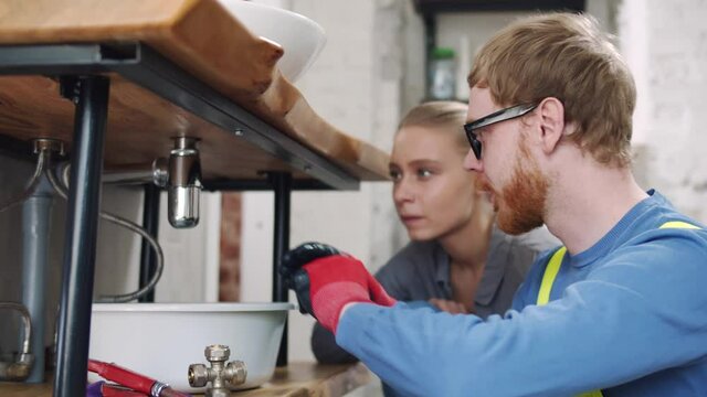 Plumber showing hopusewife how to fix pipe under sink in bathroom. Realtime