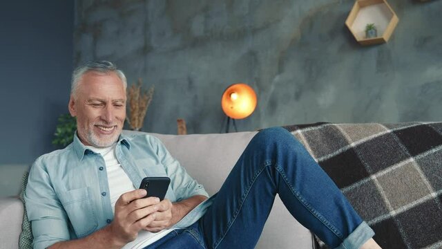 Handsome middle aged man sit divan use device post comment in living room