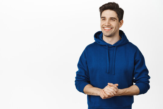 People And Emotions Concept. Smiling Caucasian Man Standing In Customer Service Pose, Holding Hands Together And Looking Aside, Ready To Help, White Background