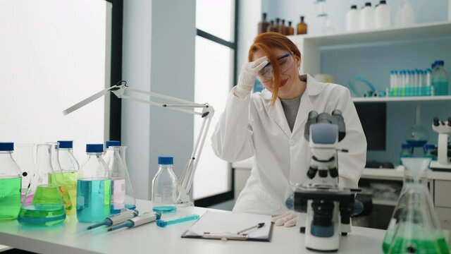 Young redhead woman wearing scientist uniform working exhausted at laboratory