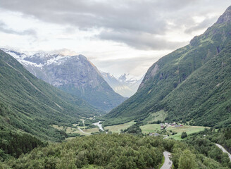 Fototapeta na wymiar Norwegian landscape with green valley between mountains with snow peaks.