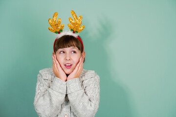 Studio portrait of suprised child girl wearing yellow deer horns isolated on mint background