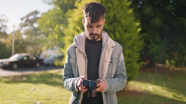 Young hispanic man standing with serious expression using camera at park