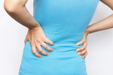 Cropped shot of a young woman in a blue t-shirt holding her lower back with her hands isolated on a white background. Back pain. Sciatica, osteochondrosis, gallstone disease, pancreatitis
