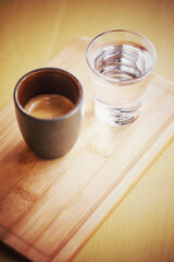 Espresso coffee in a small cup on a wooden tray beside a glass of clear water