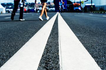 Road markings are double continuous lane on an asphalt road. Feet of pedestrians crossing the...