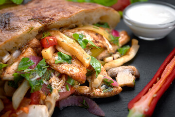 Giros, pita with chicken, sauce and vegetables, on a dark background