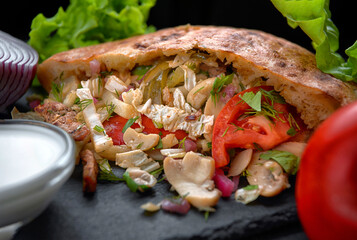 Giros, pita with pork meat, mushrooms, sauce and vegetables, on a dark background
