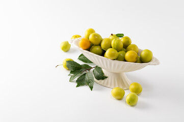yellow freshly torn cherry plum with green leaves in a ceramic vase on a white background, empty space for text