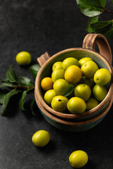 yellow freshly torn cherry plum with green leaves in ceramic cups on a gray background, close-up