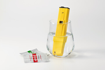pH meter in a glass of water on a white background. Measuring the characteristics of drinking water. Hardness of water. Drinking water quality analyzer showing the level of dissolved solids