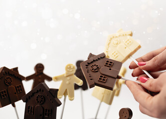 Female hands hold figurines of people and houses made of handmade chocolate, family concept. On a white background with lights in the background
