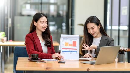 Two Young Asian businesswoman discuss with new startup project Idea presentation, analyze planning and financial statistics graph and investment market at office.