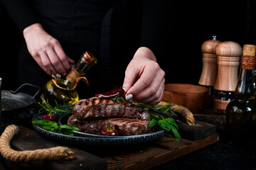 Two grilled ribeye beef steak on a plate in the hands of the chef. Food banner. On a black...