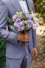 Groom in Very Peri suit holding in hands wedding bouquet, close-up. Man getting ready in the morning. Trendy color of the year 2022 in clothing.