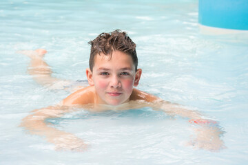 A happy boy lies in the water park in the pool.