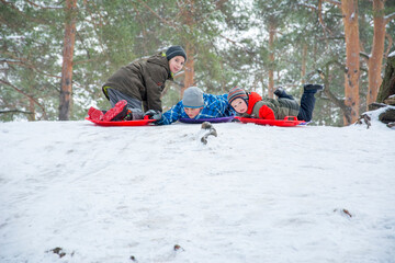 Fototapeta na wymiar In winter, in the forest, children ride downhill on plastic plates.