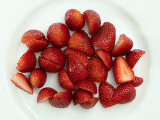 Fresh, raw, washed and ready-to-eat strawberries are on the white plate, some have been cut in half. White background.