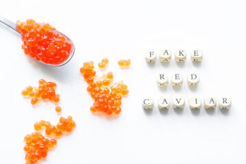 Fake red caviar eggs on white surface next to fake red caviar lettering. The concept of selling...