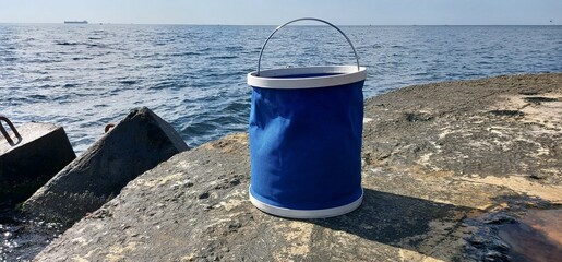 A soft blue plastic bucket for fishing against the backdrop of a calm sea.