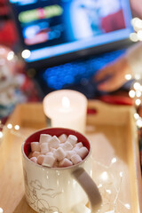 cup of cocoa and marshmallow and burning candle on plaid and a laptop with movie or work at mobile home trailer. concept camping and relaxing on new year and christmas eve